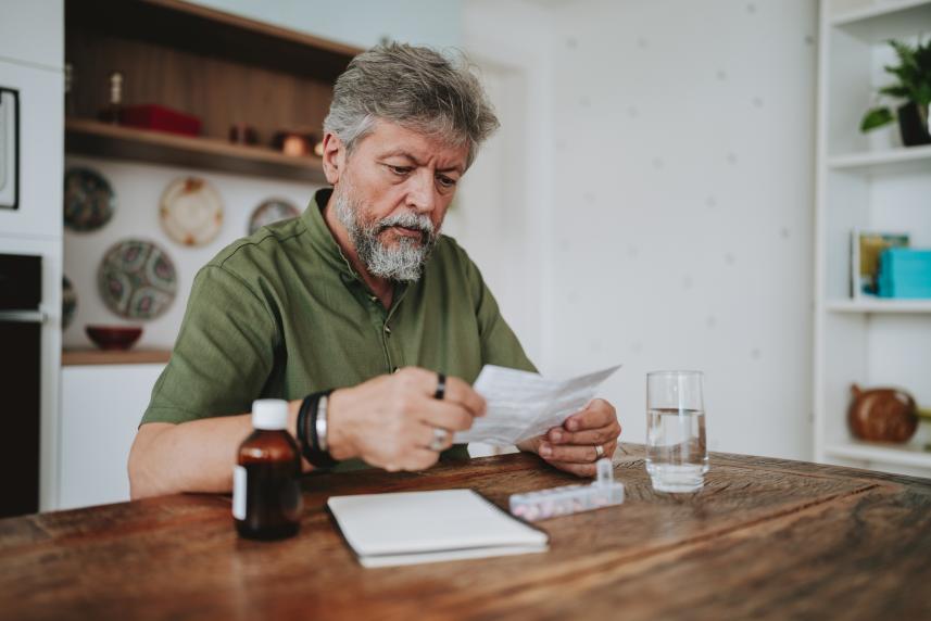 A man in a green shirt sits at his kitchen table and reviews medical terms ahead of an appointment.