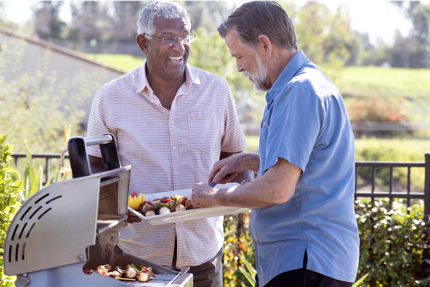 A man talking to a friend getting food off a grill